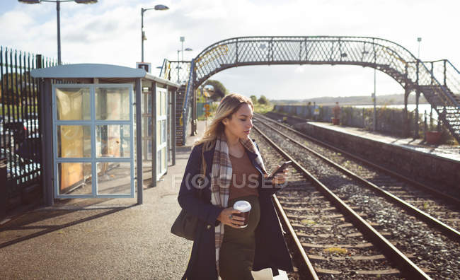 Pregnant woman using mobile phone on platform at railway station — Stock Photo