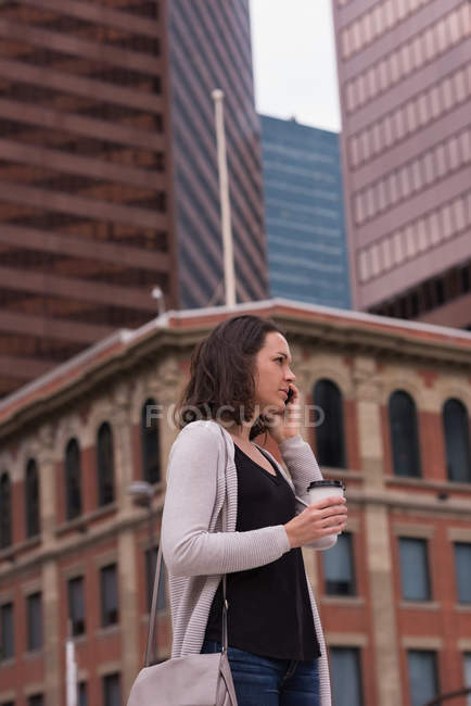 Woman having coffee while talking on mobile phone in the city — Stock Photo
