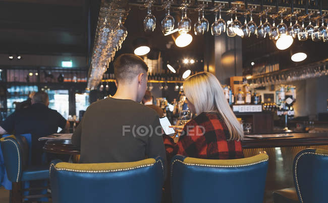 Vista trasera de la pareja discutiendo en el teléfono móvil en el mostrador de bar - foto de stock