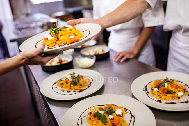 Chefs segurando comida em um prato na cozinha — Fotografia de Stock