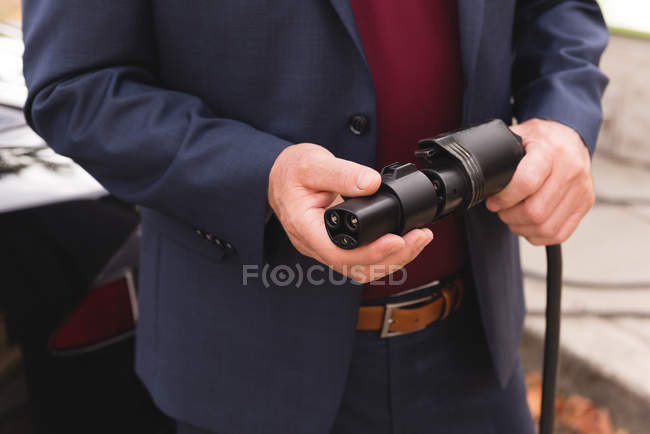 Mid section of businessman holding plug of charger at charging station — Stock Photo
