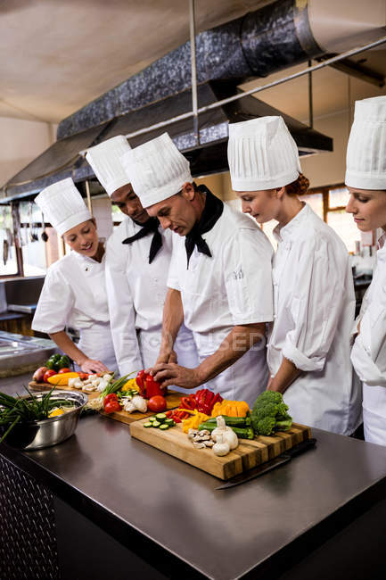 Chef cuisinier enseignant à son équipe à couper des légumes dans la cuisine — Photo de stock