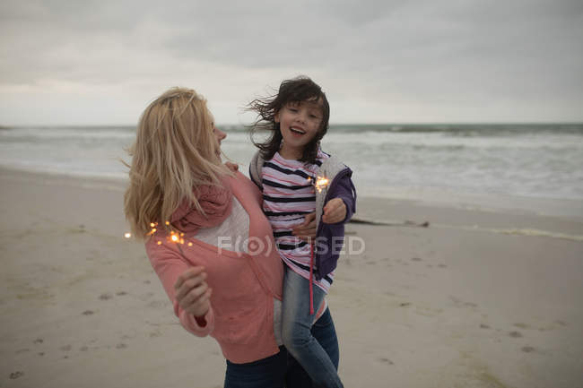 Felice madre e figlia che tengono scintille in spiaggia — Foto stock