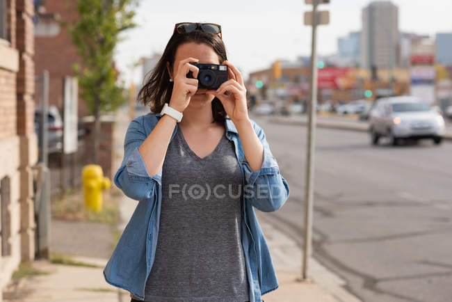 Женщина щёлкает фотографиями с камерой в городе в солнечный день — стоковое фото