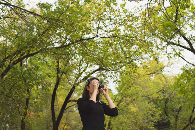 Femme en cliquant sur les photos avec appareil photo dans le parc — Photo de stock