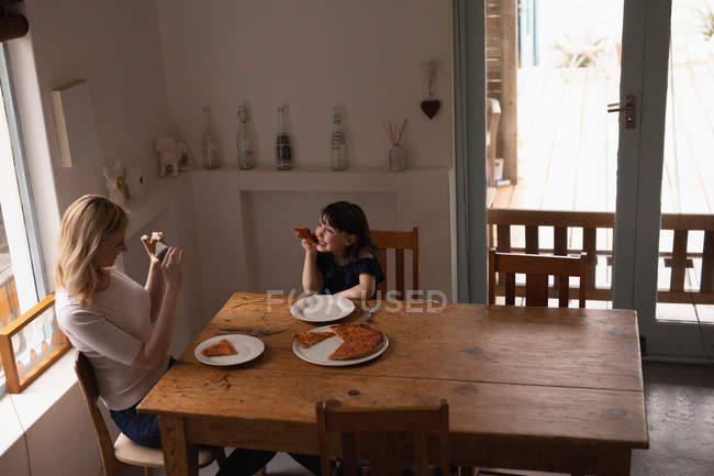 Mother clicking photo of her daughter while having food at home — Stock Photo