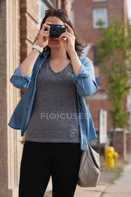Frau klickt an einem sonnigen Tag mit Kamera in der Stadt auf Fotos — Stockfoto