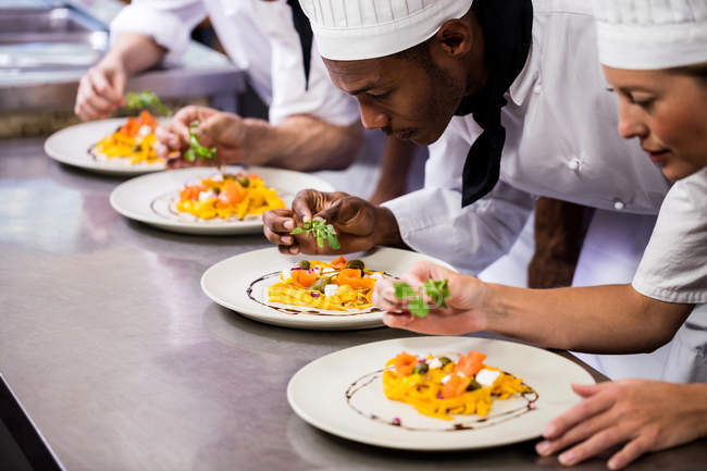 Group of chef garnishing food on plates — Stock Photo