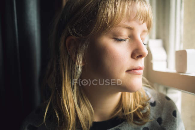Крупним планом жінка з закритими очима сидить біля вікна — стокове фото