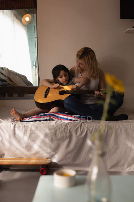 Madre e hija tocando la guitarra en el dormitorio en casa - foto de stock