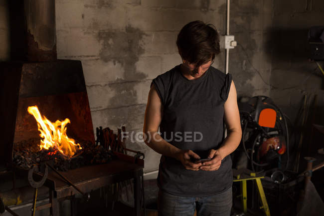 Junge Metallschmiedin benutzt Handy in Fabrik — Stockfoto