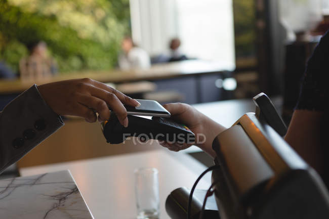 Close-up da mulher que paga com telefone celular através da tecnologia NFC no balcão de caixa — Fotografia de Stock