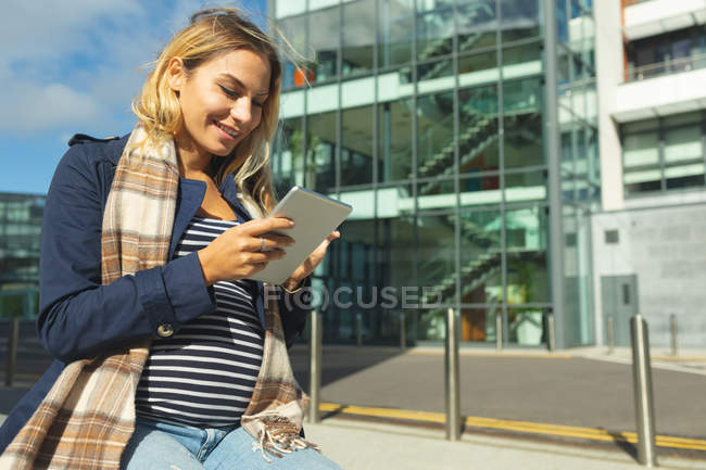 Беременная женщина, использующая цифровой планшет в городе в солнечный день — стоковое фото