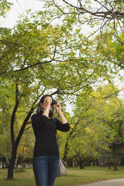 Mulher clicando fotos com câmera no parque — Fotografia de Stock