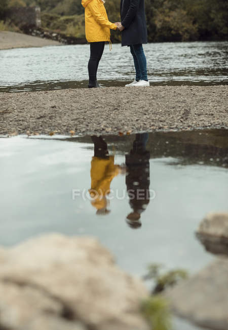 Section basse du couple tenant la main près de la rivière — Photo de stock