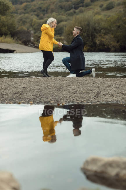 Young man proposing to woman near river — Stock Photo