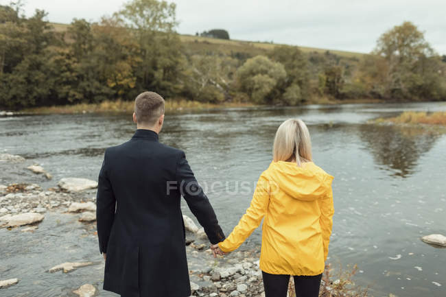 Visão traseira do casal de mãos dadas e de pé perto do rio — Fotografia de Stock