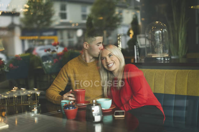Молодой человек целует женщину лоб в кафе — стоковое фото