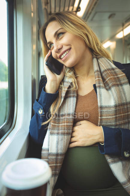 Nahaufnahme einer schwangeren Frau, die während einer Zugfahrt mit dem Handy telefoniert — Stockfoto