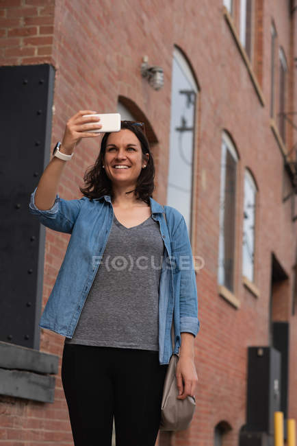 Woman clicking photos with mobile phone in the city on a sunny day — Stock Photo
