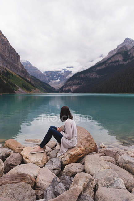 Seitenansicht einer Frau, die am Seeufer auf einem Felsen sitzt — Stockfoto