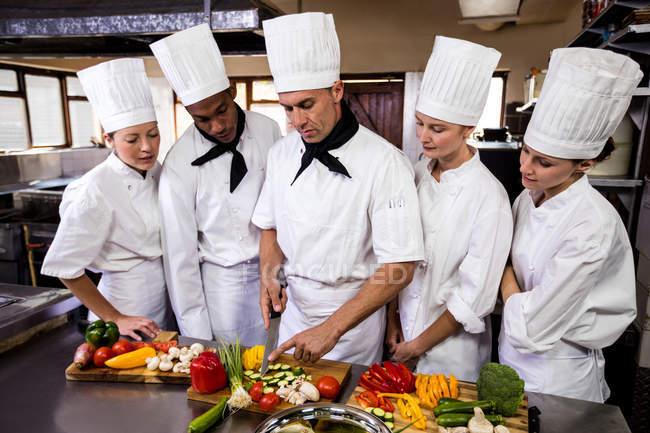 Chef cuisinier enseignant à son équipe à couper des légumes dans la cuisine — Photo de stock