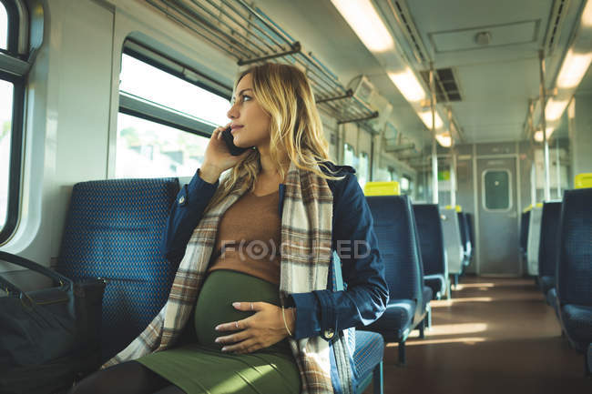 Красива вагітна жінка розмовляє по мобільному телефону під час подорожі в поїзді — стокове фото