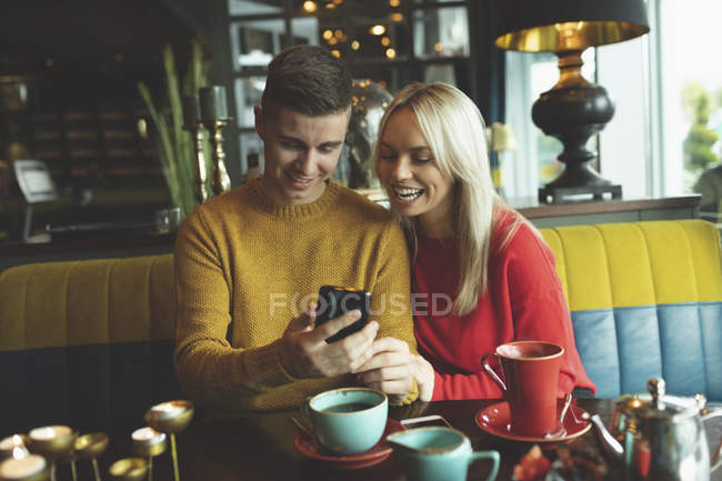 Casal olhando para o telefone celular no café — Fotografia de Stock