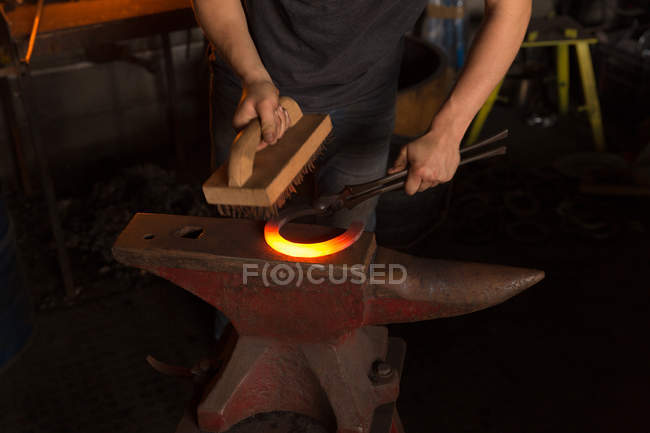 Mid section of female metalsmith brushing horseshoe in factory — Stock Photo
