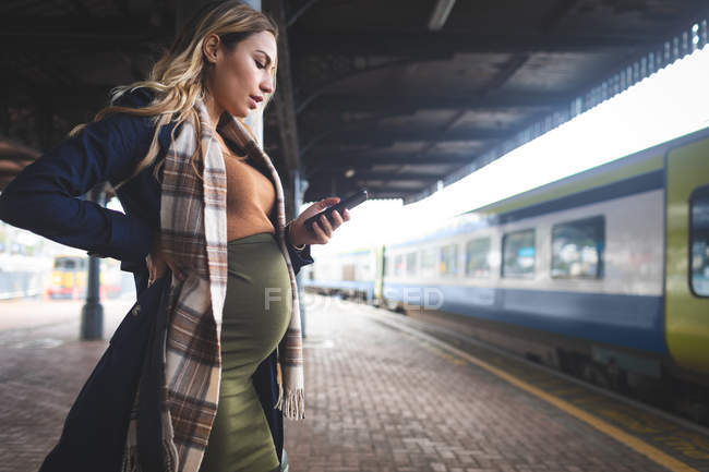Vista lateral da mulher grávida usando telefone celular na estação ferroviária — Fotografia de Stock