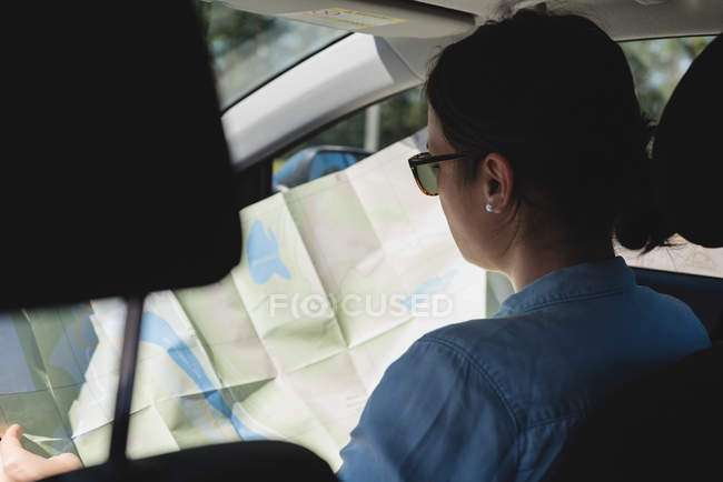 Rückansicht einer Frau, die im Auto auf die Landkarte schaut — Stockfoto