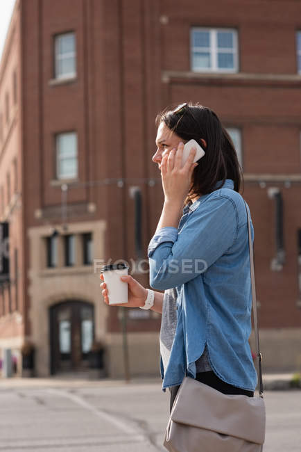 Femme prenant un café tout en parlant sur un téléphone portable dans la ville — Photo de stock