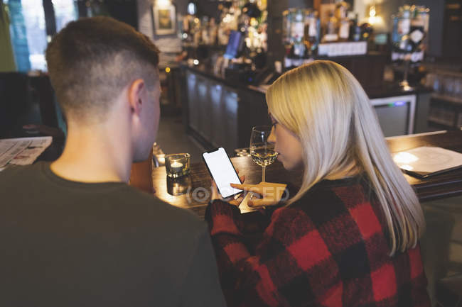 Visão traseira do casal discutindo no celular no balcão do bar — Fotografia de Stock