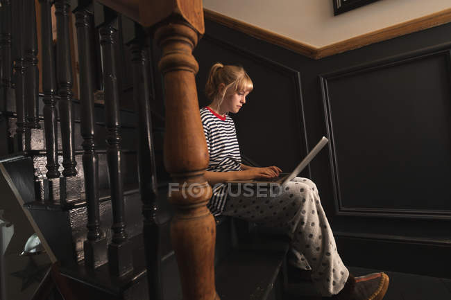 Вид сбоку на женщину, использующую ноутбук на лестнице дома — стоковое фото