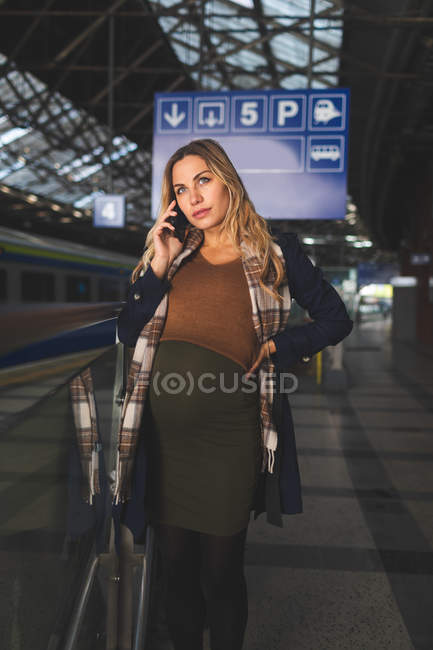 Mulher grávida conversando no telefone celular na estação ferroviária — Fotografia de Stock