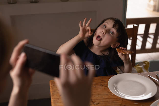 Mother clicking photo of her daughter while having food at home — Stock Photo