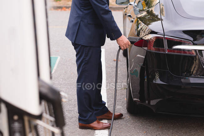 Basse section de l'homme d'affaires charge voiture électrique à la station de recharge — Photo de stock