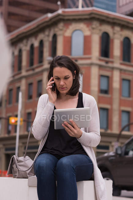 Жінка використовує цифровий планшет під час розмови на мобільному телефоні в місті — стокове фото