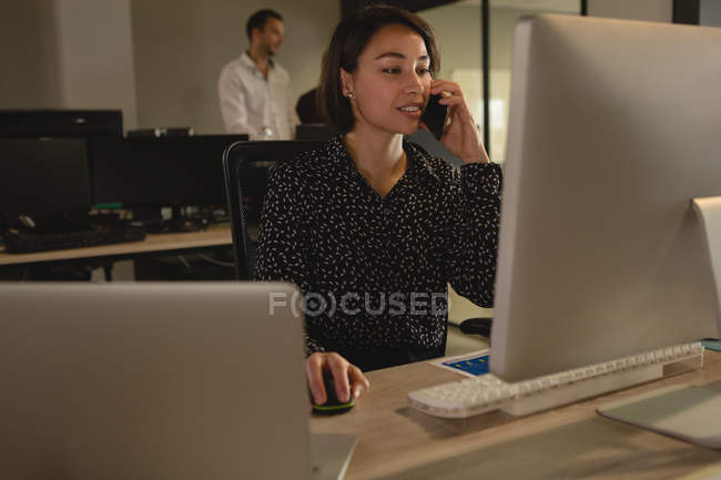 Ejecutivo hablando por teléfono móvil mientras trabaja en el escritorio en la oficina - foto de stock