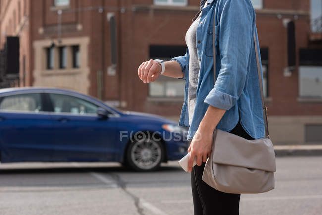 Partie médiane de la femme vérifiant le temps sur smartwatch dans la rue de la ville — Photo de stock