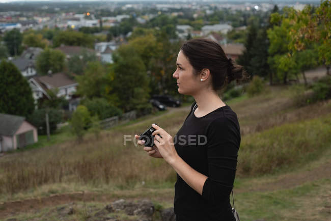 Mulher atenciosa segurando uma câmera em uma colina — Fotografia de Stock