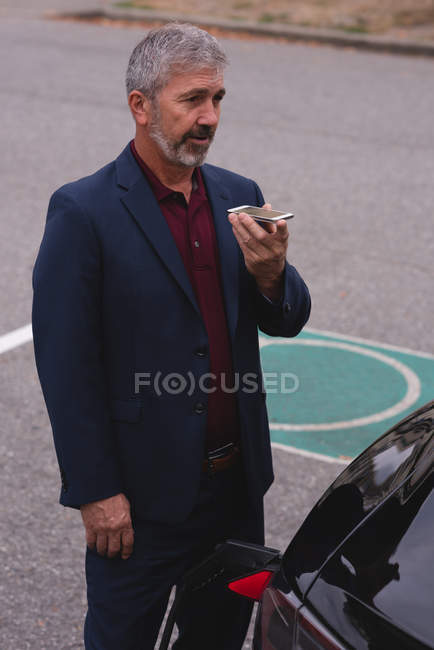 Зрілий бізнесмен розмовляє на мобільному телефоні під час зарядки електромобіля — стокове фото