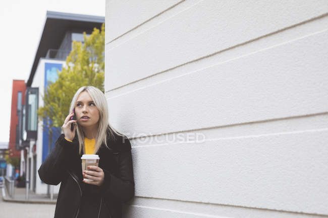 Чудова жінка розмовляє на мобільному телефоні, маючи каву — стокове фото