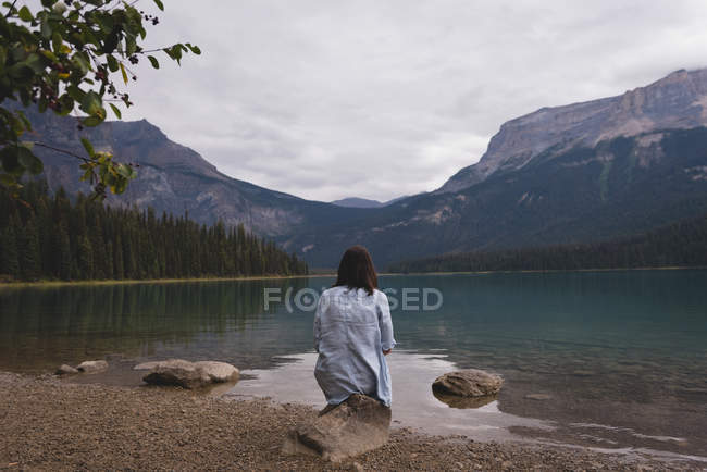 Vue arrière de la femme assise près du lac — Photo de stock