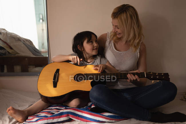 Мать и дочь играют на гитаре в спальне дома — стоковое фото