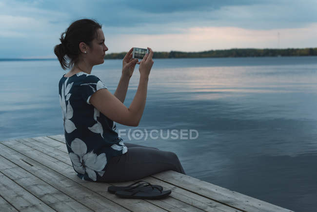 Vista lateral de la mujer haciendo clic fotos con la cámara cerca de la orilla del río - foto de stock