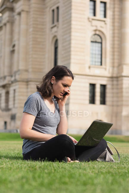 Frau benutzt Laptop beim Handy-Telefonieren im Park — Stockfoto