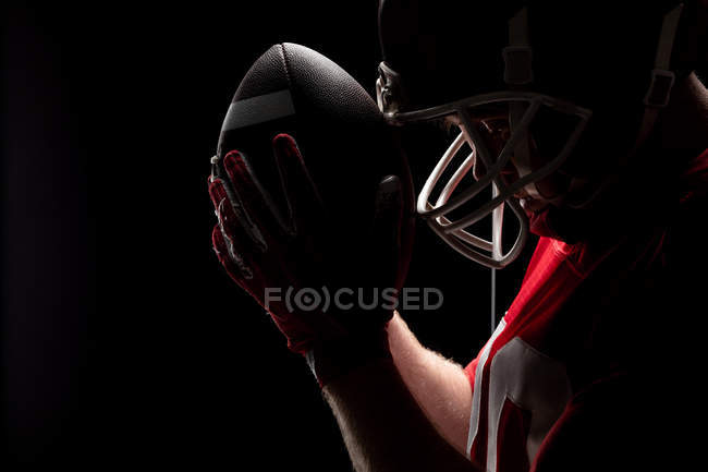 Primer plano del jugador de fútbol americano de pie con casco de rugby y pelota - foto de stock