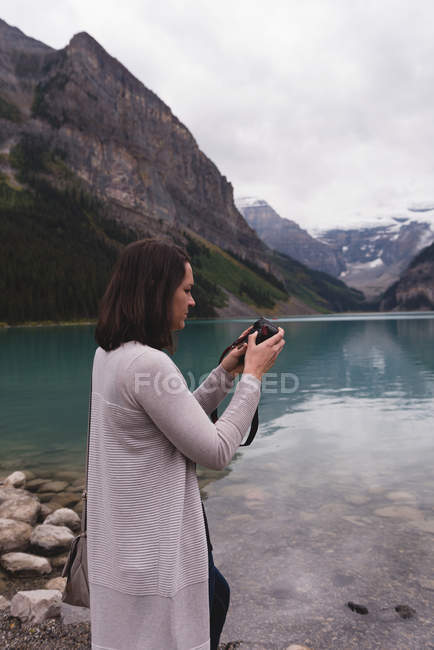 Вид збоку жінки, що переглядає фотографії на камеру біля озера — стокове фото