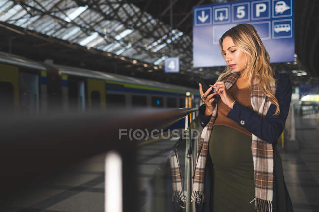 Mulher grávida bonita usando telefone celular na estação ferroviária — Fotografia de Stock